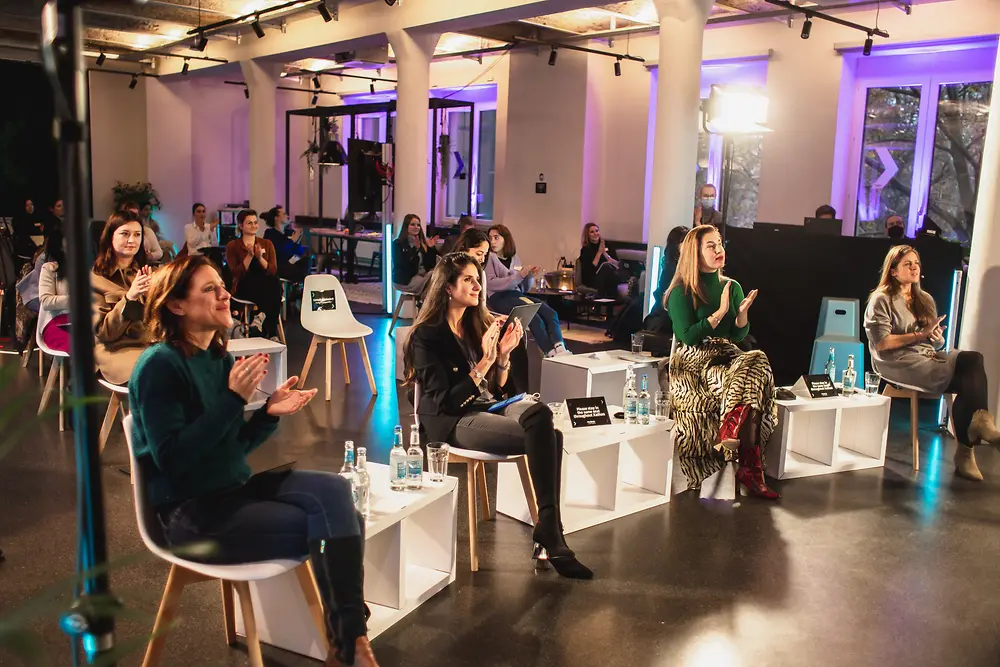 Many women sitting together in a large room and applauding.