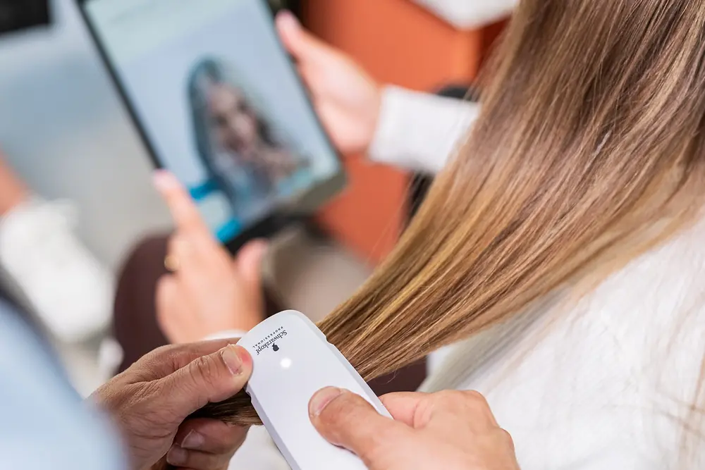 The hairdresser scans the customer's hair with the SalonLab Analyzer while she holds a tablet in her hand.