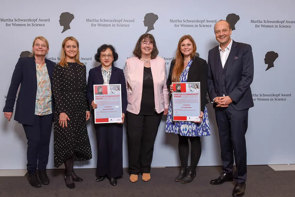 Four Henkel representatives and the two winners of the Martha Schwarzkopf Award are standing next to each other in front of the photo wall. 