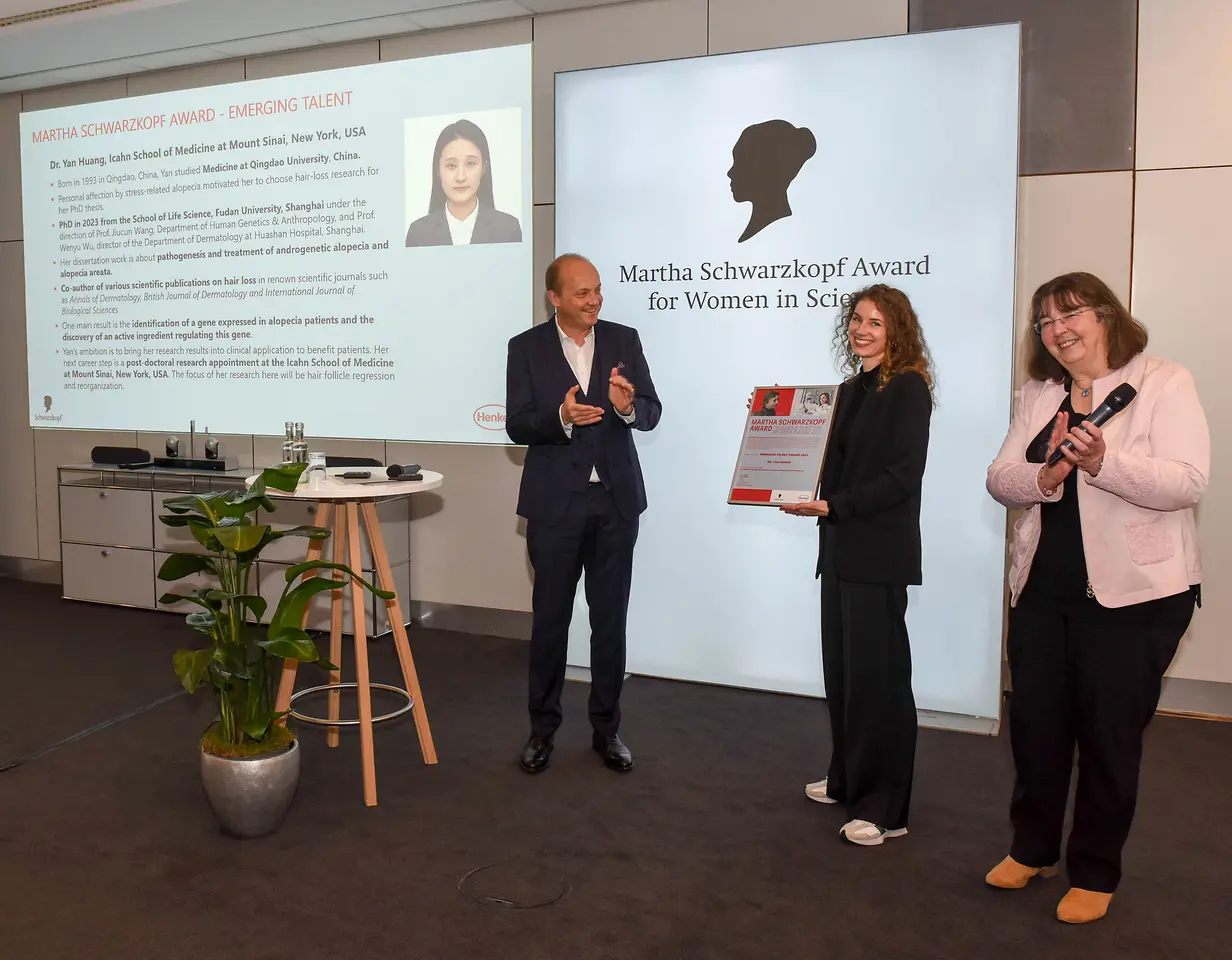 A man on the left and a woman on the right are applauding while another woman in the middle holds Dr. Yan Huang's winner's certificate. 